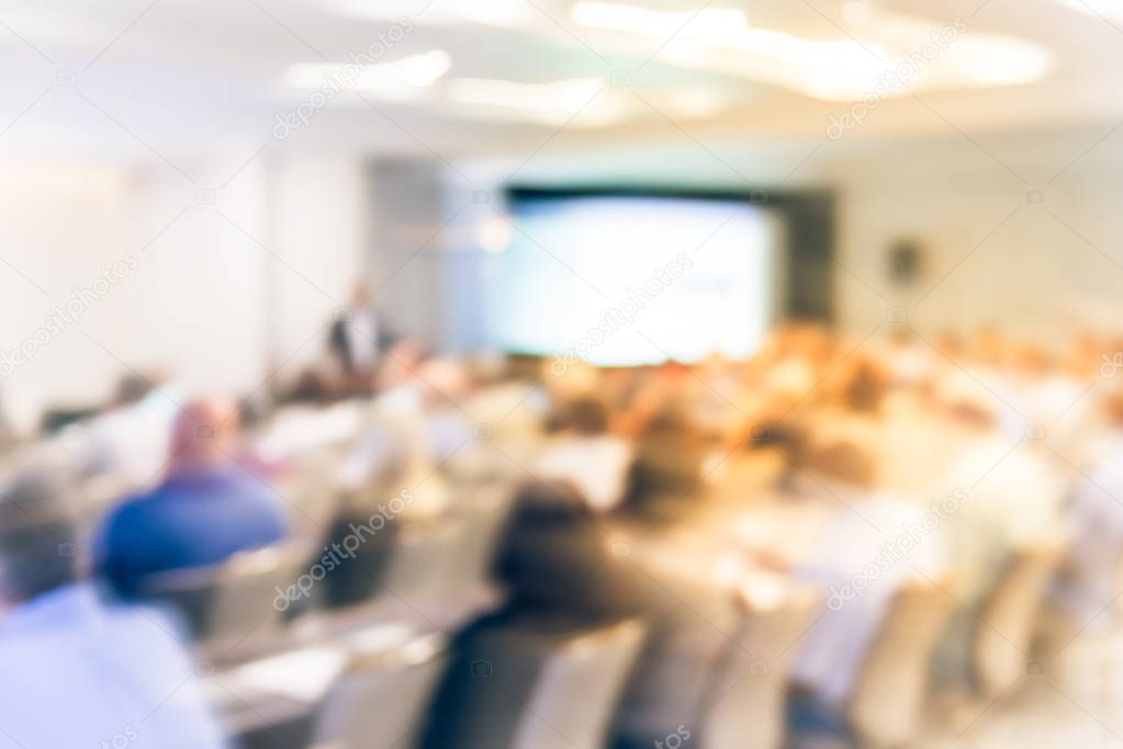 Blurred business seminar meeting with LED projector screen and speaker speech on stage. Defocused rear view audience in conference hall room, listening talk show in USA. Education, business concept