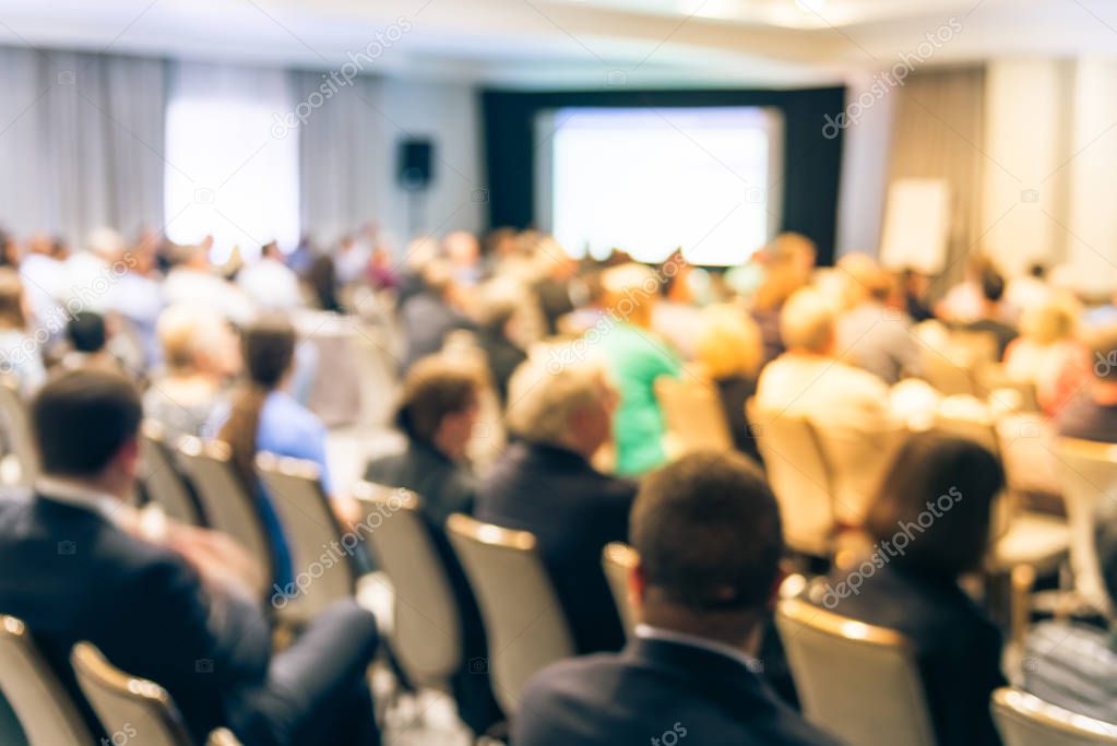 Blurred business seminar meeting with LED projector screen and speaker speech on stage. Defocused rear view audience in conference hall room, listening talk show in USA. Education, business concept