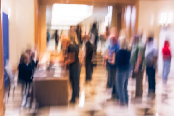 Abstract blurred participants queue line and check-in at registration table of business workshop in America. Multiethnic people sign-up and received instruction, event package from support staff