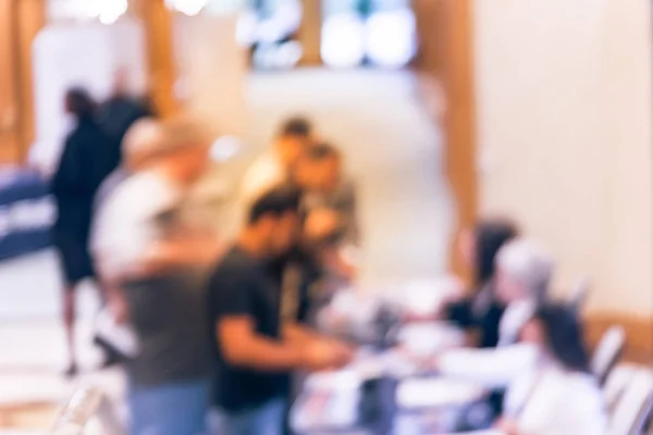 Blurred image side view diverse participants at registration check-in workshop table. Multiethnic people sign-up at conference hotel lobby and received instruction, event package from support staff