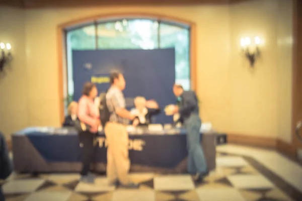 Motion blurred rear view diverse participants at registration check-in workshop table. Multiethnic people sign-up at conference hotel lobby and received instruction, event package from support staff