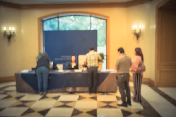 Abstract blurred rear view group of participants queue and check-in at registration table of workshop in America. Multiethnic people sign-up and received instruction, event package from support staff