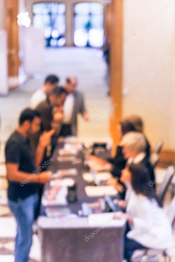 Abstract blurred participants queue line and check-in at registration table of business workshop in America. Multiethnic people sign-up and received instruction, event package from support staff