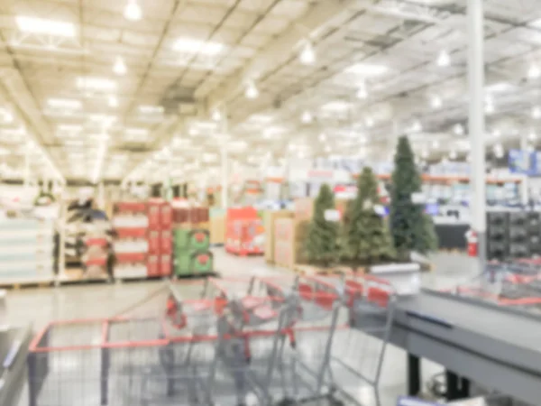 Abstract blurred row of shopping carts and huge Christmas trees decoration in background at wholesale store in US. Defocused wreaths, strings of bokeh lights surround artificial Xmas tree in warehouse