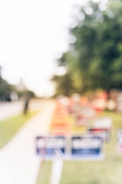 Motion blurred people walking on residential street near yard sign at for primary election day in Dallas, Texas, USA. Signs greeting early voters. clipart