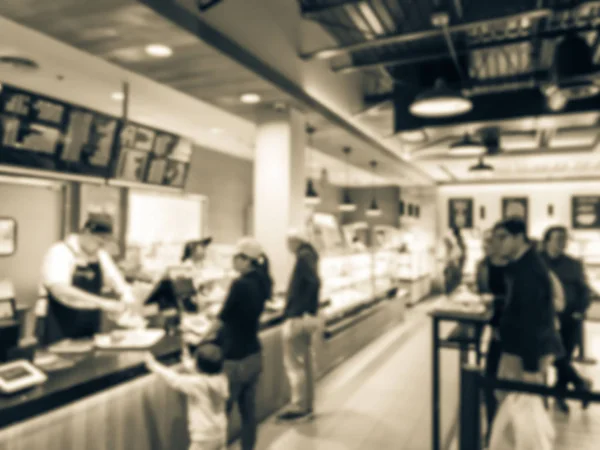 Blurred image customer checkout at Asian bakery shop and waiting in long line behind stanchion barriers. Abstract diverse multiethnic people waiting at bakehouse in America