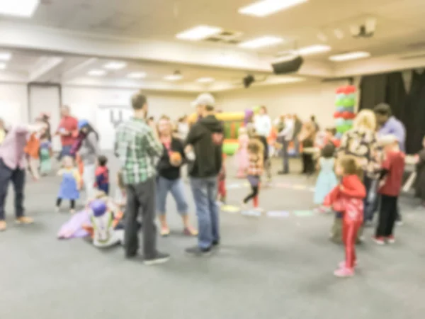 Blurred abstract kids and parents enjoy indoor Halloween party at school in Texas, America. Defocused children with costumes at fall fun games, shape links
