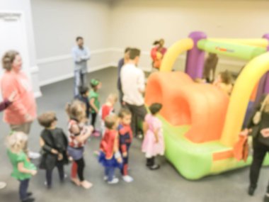 Bulanık hareket farklı çok ırklı çocuklar oyun atlama şişme sıçrama ev zevk. Ebeveynler ve çocuklar kapalı okulda Cadılar Bayramı partisi Texas, Amerika defocused