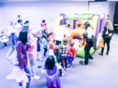 Bulanık hareket farklı çok ırklı çocuklar oyun atlama şişme sıçrama ev zevk. Ebeveynler ve çocuklar kapalı okulda Cadılar Bayramı partisi Texas, Amerika defocused