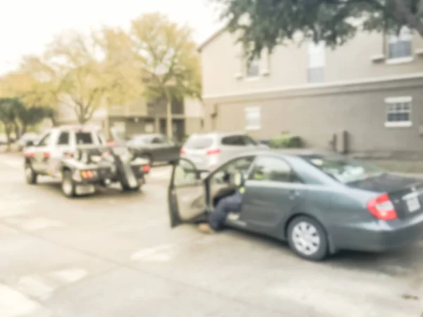 Motion blurred tow truck driver towing a damaged car from apartment building complex in Texas, America. Insurance theme concept, roadside assistance accident support
