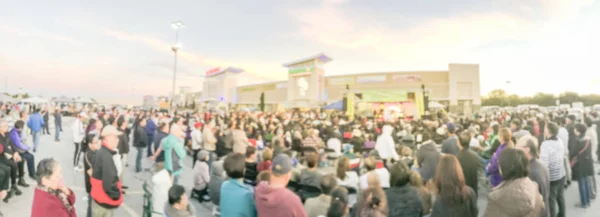 Panorama view blurred motion crowd people standing and sitting on foldable camping chair at open air stage. Defocused large group of Asian audience enjoy themselves at outdoor music festival at sunset