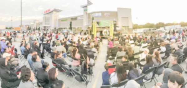 Panorama view blurred motion crowd people standing and sitting on foldable camping chair at open air stage. Defocused large group of Asian audience enjoy themselves at outdoor music festival at sunset