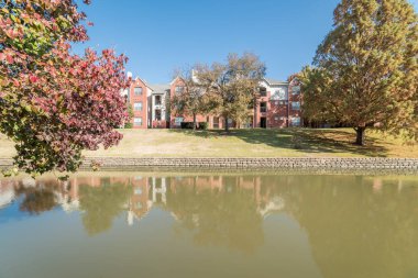 Renkli sonbahar yaprakları ağaçların Irving, Texas, ABD tarafından çevrili tipik multistorey nehir kenarında daire konut kompleksi güzel ayna yansıması.