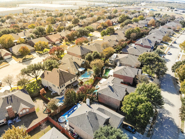 Top view typical residential neighborhood near business park in Flower Mound, northwest of Dallas, Texas, USA. Row of single family houses, colorful fall foliage color, row of warehouses in background