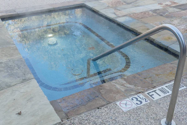 Hot outdoor Jacuzzi pool with handrail and depth signs at apartment building in Texas, America