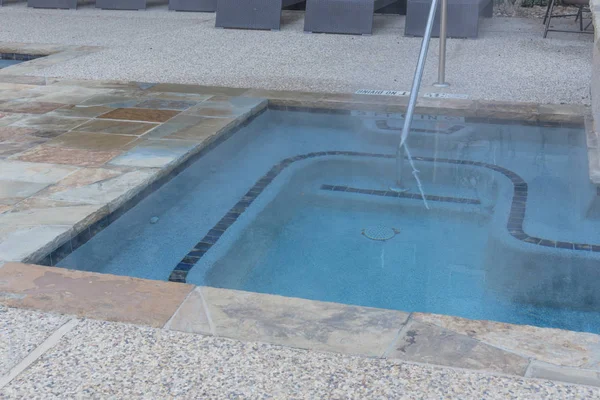 Jacuzzi pool with handrail and depth signs at apartment building in Texas, America. Row of rattan lounge pool chairs in background