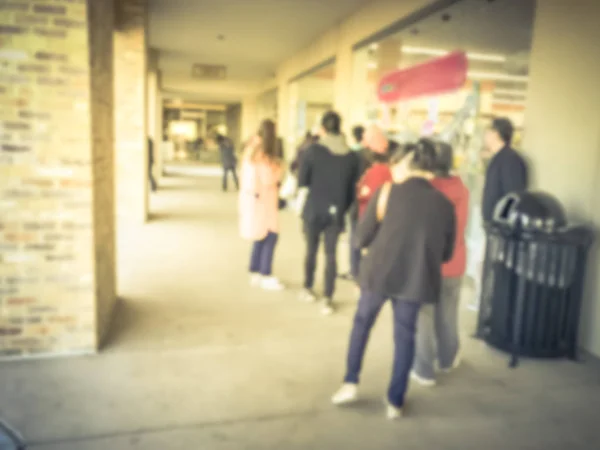 Vintage tone blurred crowd of people waiting in line for store opening Black Friday hour in Carrollton, Texas, USA. Defocused abstract shoppers standing outside a department store for shopping deals