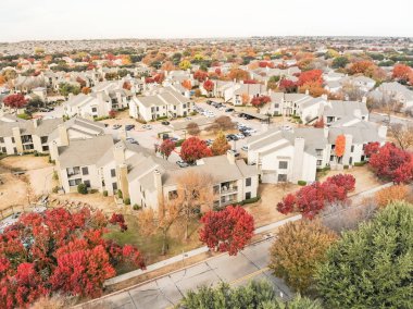 Beautiful aerial view of apartment complex near local street with sidewalk surrounded by colorful autumn leaves. Flyover rental housing subdivided unit flats near Dallas, Texas, USA clipart