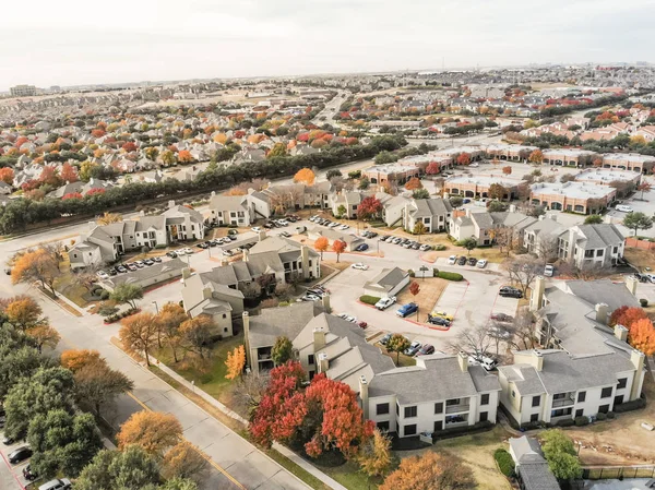 Beautiful aerial view of apartment complex near local street with sidewalk surrounded by colorful autumn leaves. Flyover rental housing subdivided unit flats near Dallas, Texas, USA