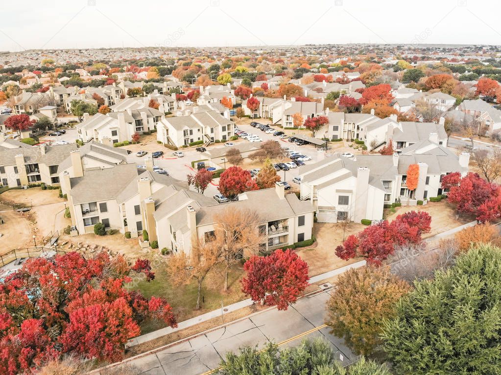 Beautiful aerial view of apartment complex near local street with sidewalk surrounded by colorful autumn leaves. Flyover rental housing subdivided unit flats near Dallas, Texas, USA