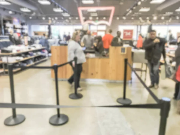 Blurred motion long line of diverse customers waiting to checkout at apparel, accessories store in Texas, USA. Defocused abstract crowed people retractable stanchions queue barrier, holiday shopping