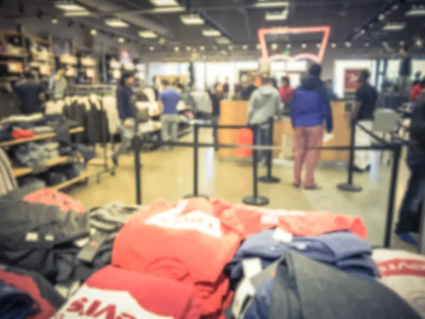 Blurred motion long line of diverse customers waiting to checkout at apparel, accessories store in Texas, USA. Defocused abstract crowed people retractable stanchions queue barrier, holiday shopping