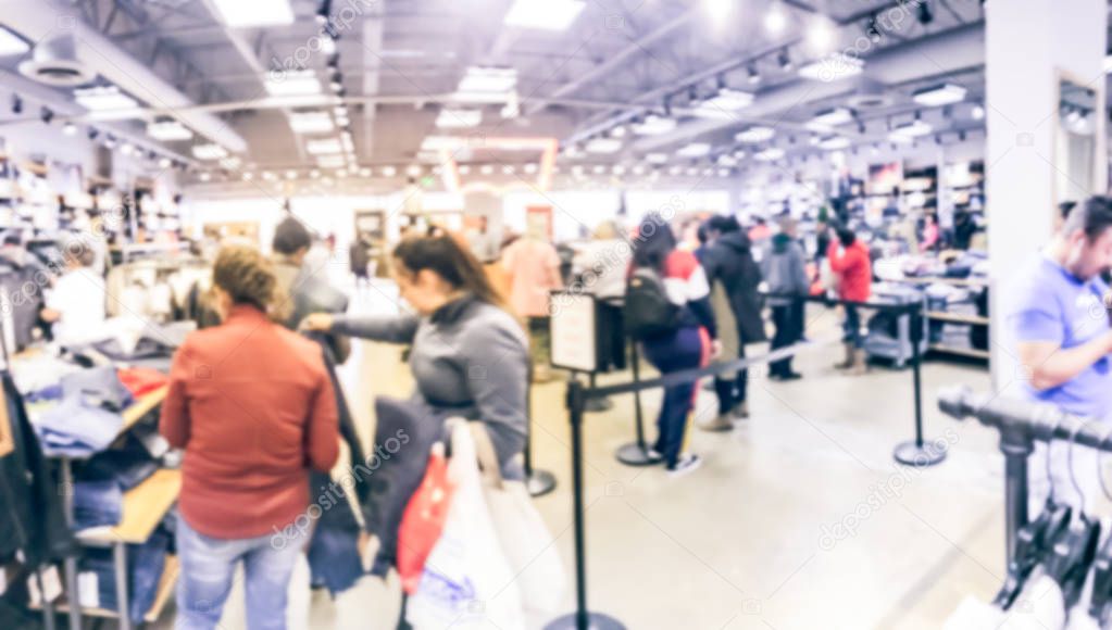 Blurred motion long line of diverse customers waiting to checkout at apparel, accessories store in Texas, USA. Defocused abstract crowed people retractable stanchions queue barrier, holiday shopping
