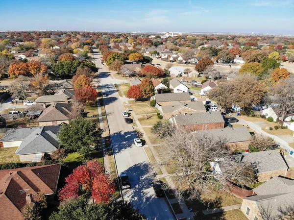 Top view beautiful neighborhood in Coppell, Texas, USA in autumn season. Row of single-family home with attached garage, garden, surrounded by colorful fall foliage leaves under blue sky