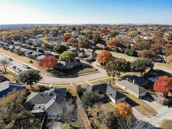 Top view beautiful neighborhood in Coppell, Texas, USA in autumn season. Row of single-family home with attached garage, garden, surrounded by colorful fall foliage leaves under blue sky