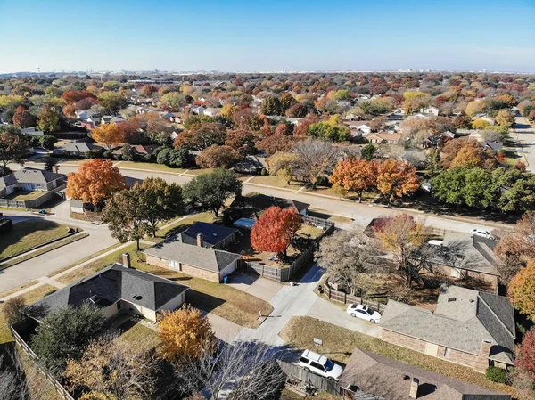 Top view beautiful neighborhood in Coppell, Texas, USA in autumn season. Row of single-family home with attached garage, garden, surrounded by colorful fall foliage leaves under blue sky