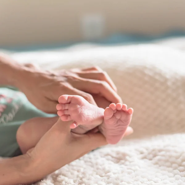 Close-up little pink toes of newborn Asian baby in his mom hands with cozy blanket background. Love, family and protection concept