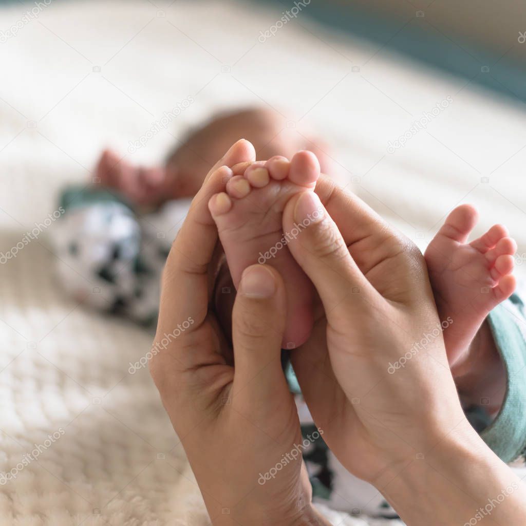 Little toes of newborn Asian baby in his mom hands. Love and protection concept