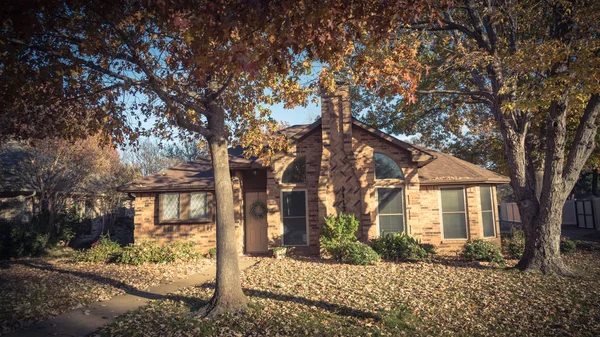 Entrance of single-family house with colorful autumn leaves in Flower Mound, Texas, USA. Porch and bay windows with seasonal wreath on sunny fall day with leaves on the ground