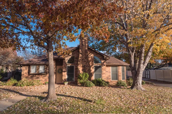 Entrance of single-family house with colorful autumn leaves in Flower Mound, Texas, USA. Porch and bay windows with seasonal wreath on sunny fall day with leaves on the ground
