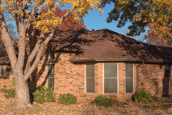 Typical single-family house at street corner with colorful autumn leaves in Flower Mound, Texas, USA. One story residential house with brick house and big trees