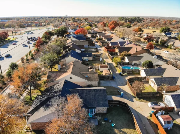 Aerial view residential neighborhood with colorful fall foliage nears in Flower Mound, Texas, USA. Flyover row of single-family houses with garden, attached garage and swimming pool