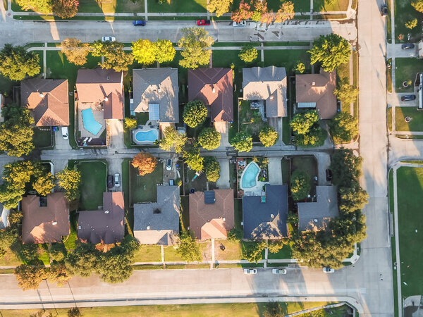 Aerial vertical view residential houses with swimming pool in Carrollton, Texas, USA during fall sunset. Top view row of single-family homes with garden, driveway and attached garage