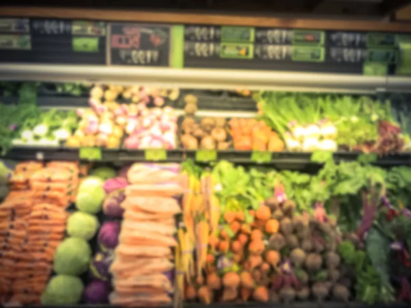 Vintage tone blurred abstract wide selection of fresh vegetable on cooler display at grocery store. Defocused background raw organic produces at supermarket shelves