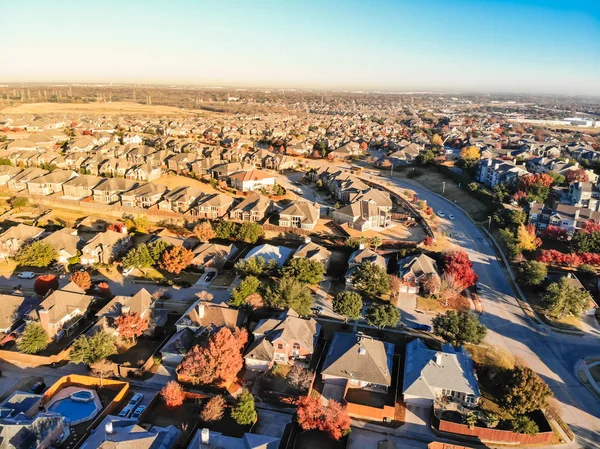 Aerial view urban sprawl with colorful fall foliage near Dallas, Texas, USA. Flyover suburban subdivision with row of residential single-family houses and apartment complex buildings in autumn morning