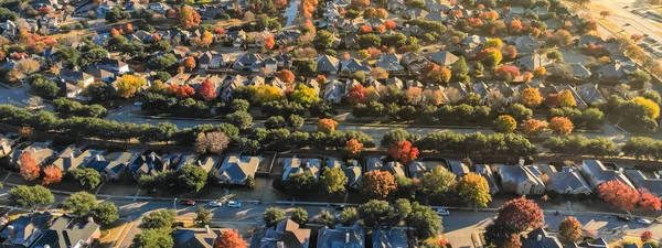 Panorama aerial view urban sprawl with colorful fall foliage near Dallas, Texas, USA. Flyover suburban subdivision with row of residential single-family houses, apartment complex buildings