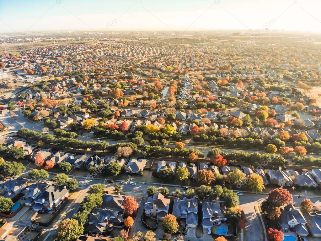 Aerial view urban sprawl with colorful fall foliage near Dallas, Texas, USA. Flyover suburban subdivision with row of residential single-family houses and apartment complex buildings in autumn morning