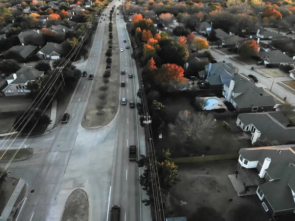 Aerial view residential neighborhood near highway with traffic at fall sunset in Flower Mound, Texas, USA. Row of single-family houses with swimming pool and colorful leaves