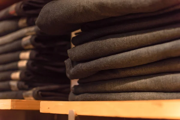 Close-up soft focus stack of blue jeans at clothing store in America. Rack fashionable denim garments, casual dress style on store shelves