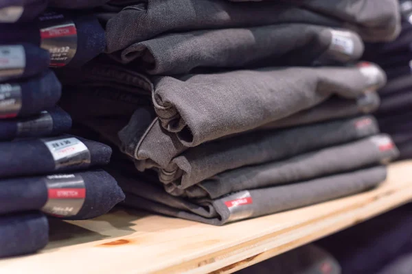 Close-up soft focus stack of blue jeans at clothing store in America. Rack fashionable denim garments, casual dress style on store shelves