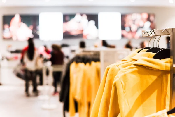 Vintage tone selective focus trending clothes hanging at clothing shop with blurred long queue of customer behind stanchion beltline at checkout counter