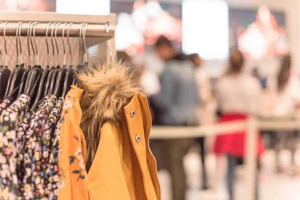 Selective focus trending clothes hanging at clothing shop with blurred long queue of customer behind stanchion beltline at checkout counter