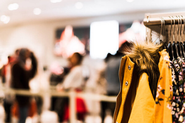 Vintage tone selective focus trending clothes hanging at clothing shop with blurred long queue of customer behind stanchion beltline at checkout counter