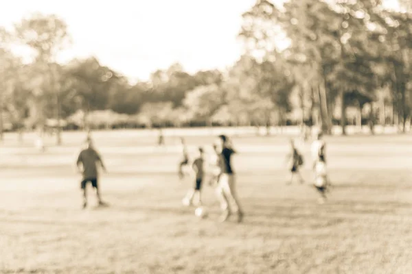 Filtered image blurry background coach playing soccer with boys at park during sunset