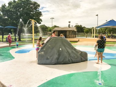 Çok kültürlü çocuklar ve ebeveyn yaz fırtınalı hava altında splash parkta oynuyor