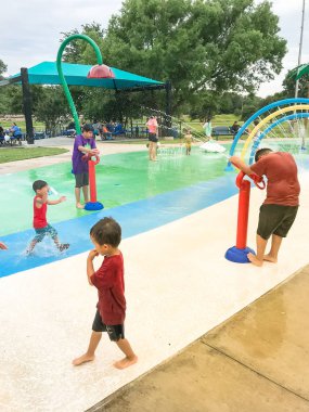Çok kültürlü çocuklar ve ebeveyn yaz fırtınalı hava altında splash parkta oynuyor